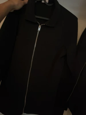 Overshirt Selected Home - En stilren svart jacka med hel dragkedja framtill och klassisk krage. Passar perfekt till vardagslooken och är enkel att matcha med olika outfits. Jackan har lång ärm och en clean design utan synliga detaljer.