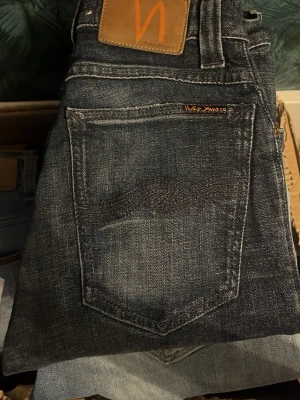 Nudie jeans  - Mörka jeans från Nudie Jeans, modell High Kai med kontrastmönster. Midja 31cm, längd 107cm. JAG SKICKAR EJ FLER BILDER NÄR JAG BÄR JEANSEN! för bättre inblick i passformen rekommenderar jag att googla på modellnamnet. För storleksguide kolla måtten noggrant då jeansen alltid kan vara uppsydda heller krympta och jag ej tar emot returer :) n6