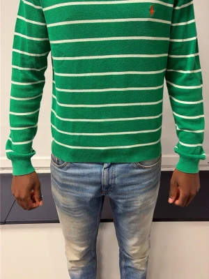 Grön randig tröja från Ralph Lauren - Snygg grön tröja med vita horisontella ränder från Ralph Lauren. Tröjan har rund halsringning, långa ärmar och en liten röd logga broderad på bröstet. Perfekt för en avslappnad och stilren look.