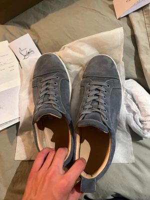 Gråa sneakers i mocka -  gråa skor Fårn lobutin i mocka med röd sula och klassisk snörning. Skorna har en låg profil och diskreta sömdetaljer. Insidan är ljusbeige och de har en dragflik bak för enkel påtagning. Perfekta för en clean och stilren look. Skirv om ni har några frågor🤗