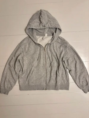 Ljusgrå zip hoodie med huva - En basic ljusgrå hoodie med dragkedja framtill och två fickor. Från HM i storlek S