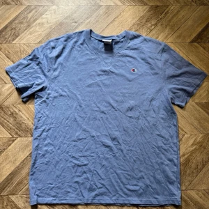 Blå t-shirt från Champion - Säljer en blå t-shirt från Champion i storlek 2XL. T-shirten har korta ärmar, rund halsringning och en liten Champion-logga broderad på bröstet. Tillverkad i mjuk bomull för en skön och avslappnad stil.