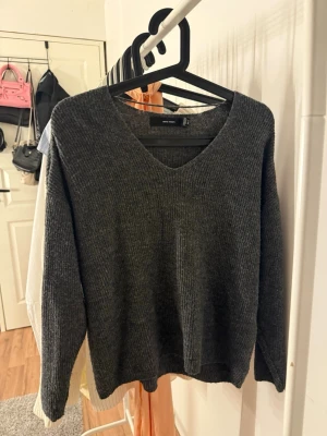 Mörkgrå stickad tröja Vero Moda - Mysig mörkgrå stickad tröja från Vero Moda med v-ringning och långa ärmar. Tröjan har en klassisk rak passform och är tillverkad i ett mjukt stickat material.