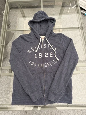 Hollister Zip-Up Hoodie | Stl S - Säljer en superfin mörkblå Hollister hoodie med dragkedja! Tryck framtill med "Hollister 1922 Los Angeles". Storlek S (60% bomull, 40% polyester). Mjuk, skön och i jättefint skick! 