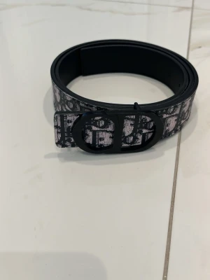 Svartvitt bälte med grafiskt mönster - Coolt svartvitt bälte med grafiskt mönster och matchande spänne. Bältet har en bred design och ett stilrent, rundat spänne som ger en modern touch. Perfekt accessoar för att ge din outfit lite edge.