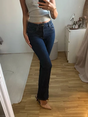 Mörkblå bootcut jeans  - Säljer ett par mörkblå bootcut jeans med hög midja och klassiska fem fickor. Jeansen har en smickrande passform och är tillverkade i ett stretchigt denimtyg som sitter snyggt på kroppen. Perfekta till en enkel topp eller hoodie