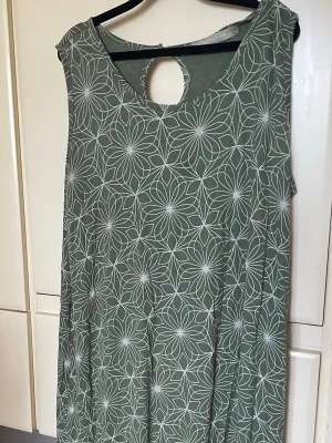 Cassiopea mönstrad grön vit stl 40 - En beg. grön klänning med ett vitt blommönster. Klänningen är ärmlös och har en rund halsringning med en liten öppning bak. Perfekt för en avslappnad stil. Företaget är Danskt och finns i Hvidovre Köpenhamn. Modehuset är KSK fashion.