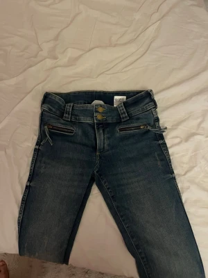 Blå skinny jeans med dragkedjor - Säljer ett par blå skinny jeans med två coola dragkedjor framtill och dubbla knappar i midjan. Jeansen har en klassisk femficksmodell och är i stretchigt denimtyg för skön passform. Perfekta till en avslappnad streetstyle-look.
