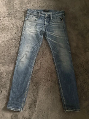 Ljusblå slim fit jeans - Säljer ett par ljusblå slim fit jeans med snygga slitningar och tvättade detaljer. Klassisk femficksmodell med dragkedja och knapp framtill. Jeansen har raka ben och är perfekta för en avslappnad stil.