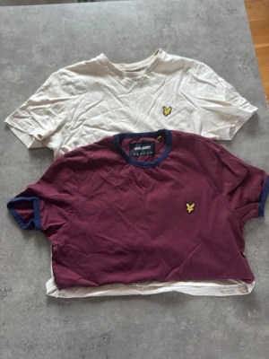Två Lyle & Scott t-shirts - Säljer två t-shirts från Lyle & Scott. En vinröd t-shirt med blå detaljer vid krage och ärmslut samt en vit t-shirt, båda med den klassiska loggan på bröstet. Perfekta för en avslappnad stil. 99kr styck 