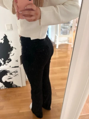 Svarta bootcut jeans med hög midja - Snygga svarta jeans med bootcut-modell och hög midja. Jeansen har en klassisk femficksdesign och sitter tight över höfterna för en smickrande siluett. Perfekta till en croppad tröja eller hoodie för en trendig look.
