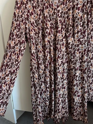 Blommig långärmad klänning/tröja - Säljer en långärmad klänning/tröja med blommigt mönster i vinrött, brunt, beige och vitt. Klänningen har v-ringning och är gjord i ett mjukt, stretchigt material. Perfekt för dig som vill ha något bekvämt men ändå snyggt. Köpt från PRIMARK, men saknar sin tagg (togs bort för irritation🤗). Endast använd 1-2 gånger. 