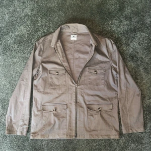Beige overshirt från John Henric - Stilren beige overshirt från John Henric med fyra stora fickor framtill och dragkedja. Tillverkad i mocka och har klassisk krage. Perfekt lager-på-lager-plagg för en avslappnad look.