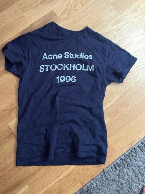 Mörkblå Acne Studios t-shirt - Snygg mörkblå t-shirt från Acne Studios med tryck 'STOCKHOLM 1996' på bröstet. Klassisk passform och rund hals. Perfekt för dig som gillar stilrena och trendiga plagg. Passar ungerfär 175-180cm