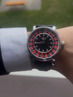 Roulette-klocka med svart läderband - Unik klocka med roulette-inspirerad urtavla i svart, rött och grönt. Klockan har ett svart läderband med klassiskt spänne och silverfärgat boett. Perfekt för dig som vill sticka ut med en cool accessoar.