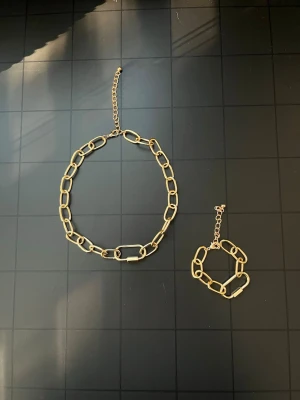 Guldfärgat chunky smyckesset – halsband & armband - Snyggt guldfärgat set med halsband och matchande armband i chunky kedjedesign. Stora ovala länkar och justerbar förlängningskedja. Statement-modell som passar både till vardags och fest.