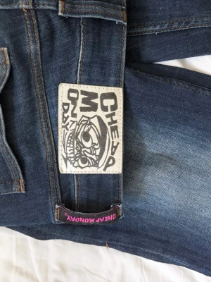 Mörkblå jeans från Cheap Monday - Säljer ett par mörkblå jeans från Cheap Monday med klassisk femficksmodell och coolt patch med logga bak. Jeansen har raka ben och snygga slitningar framtill för en avslappnad look. Materialet är denim i bomull med lite stretch.