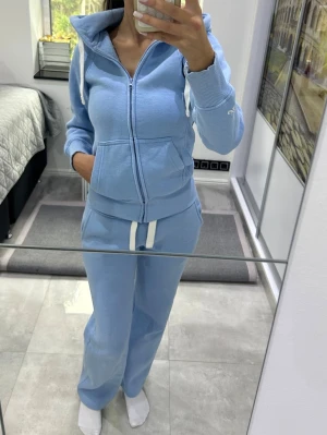 Ljusblått mjukisset med huva - Säljer ett ljusblått loungewear-set med zip-hoodie och matchande byxor. Hoodien har dragkedja, fickor och ribbade muddar. Byxorna har resår i midjan och vita dragsnören. Perfekt för chill dagar hemma eller när du vill vara bekväm.