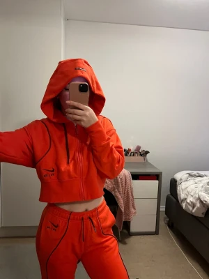 Nike Air set orange - Säljer en orange croppad hoodie med dragkedja och huva. Hoodien har svarta detaljer och snörning i huvan samt tryck på bröstet. Perfekt för en sportig och trendig look.Det är set.