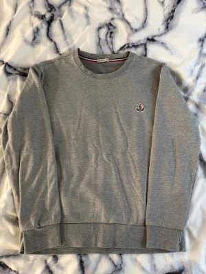Moncler tröja - Snygg grå sweatshirt från Moncler med rund halsringning och diskret Moncler-logga på bröstet. Tröjan har långa ärmar, ribbade muddar och en klassisk passform. Perfekt för en avslappnad och stilren look. Använd, mycket bra skick, storlek M men kan passa S också.