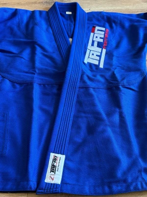 Blå Judo/BJJ-gi från TAFAN A1 - Säljer en blå kampsports-gi från TAFAN Fightwear i storlek A1. Jackan har broderad logga på bröstet och ryggen samt förstärkta sömmar. Materialet är slitstarkt och strukturerat, perfekt för judo eller brasiliansk jiu-jitsu.                                                          Brand new BJJ Gi/Kimono Brand: Tafan Fightwear Size:A1 New Unused,in Blue 🔵 Colour , Coat with Pearl Weave 450 GSM Pant with Ripstop 10 Oz Check Picture for Size Chart on the  pictures🤙