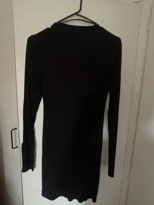 Svart långärmad klänning BikBok - En enkel och stilren svart långärmad klänning från BikBok i kort modell. Klänningen har en rund halsringning och är gjord i ett mjukt, stretchigt material som sitter snyggt på kroppen.