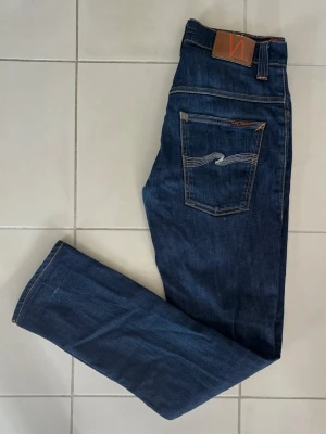 Nudie Jeans - Oerhört feta Nudie Jeans i toppskick! Exklusiva jeans med svinfeta bakfickor med vit färg på signatur mönstret. Badgen är otroligt fräsch precis som resten av jeansen. Ett måste till garderoben! Längd - 104 cm och bredd - 39 cm. 