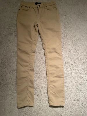 Acne studios chinos med raka ben - Snygga beige chinos med klassisk femficksdesign och raka ben. Byxorna har bälteshällor, knappgylf och är tillverkade i ett mjukt bomullstyg som ger en skön känsla. Perfekta för en clean och avslappnad stil. Från acne studios. Bra skick.