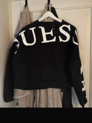 Svart sweatshirt från GUESS - Säljer en svart sweatshirt från GUESS med stor vit logga över bröstet och ärmen. Tröjan har rund halsringning och långa ärmar. Tillverkad i mjukt material som passar perfekt till en avslappnad stil.