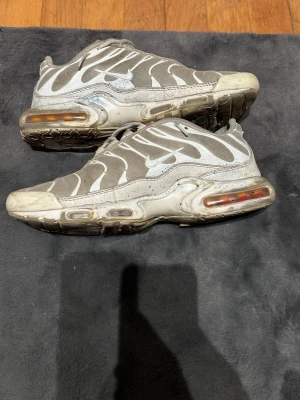 Gråvita Nike sneakers med luftdämpning - Säljer ett par gråvita Nike sneakers med tydliga vita vågmönster och synlig luftdämpning i sulan. Skorna har en sportig look med mesh- och syntetmaterial samt lågt skaft. Perfekta för dig som gillar streetwear och vill ha något bekvämt och stilrent. Skorna är väldigt använda som de syns därför en billig peng för dom som vill ha dem🙂