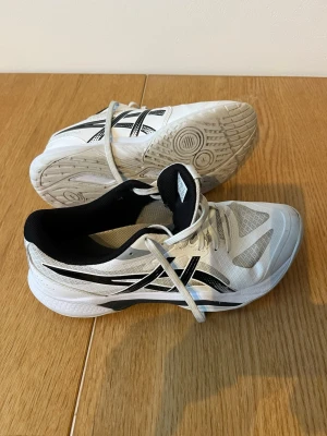 Vita Asics inomhusskor - Vita inomhusskor  från Asics med svarta detaljer. Skorna har snörning, vadderad häl och slitstark yttersula. Använda en vinter som handbollsskor. Kostade mer än 1000kr vid inköp. 