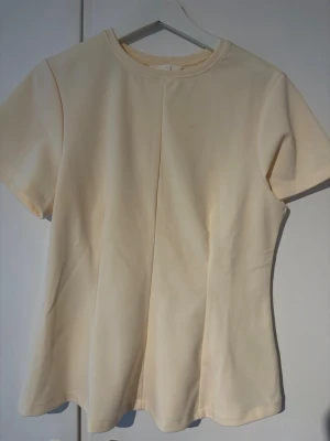 Ljusgul basic t-shirt med rund hals - En enkel och stilren ljusgul t-shirt med rund halsringning och korta ärmar. T-shirten har en figursydd passform och är tillverkad i mjukt bomullsmaterial, perfekt för en clean och avslappnad look. Endast använd en gång.