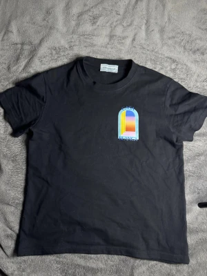 Svart Casa Blanca t-shirt med tryck - Svart t-shirt med färgglatt grafiskt tryck fram och stort tryck bak med texten 'Casa Blanca'. T-shirten har rund hals och korta ärmar. Materialet ser ut att vara mjuk bomull och passformen är normal.