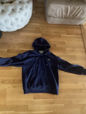 Mörkblå hoodie från Lacoste - Snygg mörkblå hoodie från Lacoste med klassisk krokodillogo på bröstet. Hoodien har huva med dragsko och en stor magficka framtill. Tillverkad i mjukt material som känns skönt mot huden. Perfekt för en avslappnad och stilren look. Använd 3 gånger ingen skada ingeting. Priset kan diskuteras!