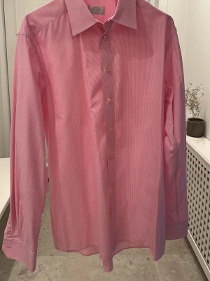 Rosa rutig skjorta från Eton - Säljer en klassisk rosa skjorta från Eton med diskret rutigt mönster. Skjortan har lång ärm, knappar framtill och en snygg krage. Perfekt för dig som gillar stilrena och tidlösa plagg. Tillverkad i bomull för en skön känsla. 
