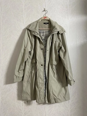 Beige/Khaki Isolde Regnjacka - Säljer en beige/khaki regnjacka med vackert foder. Jackan har använts flitigt och har vissa skavanker som framför allt syns i snörningarna, annars i bra skick. Den har många praktiska fickor med knapp och dragkedja, samt en justerbar midja. Passar perfekt till höst/vår. 
