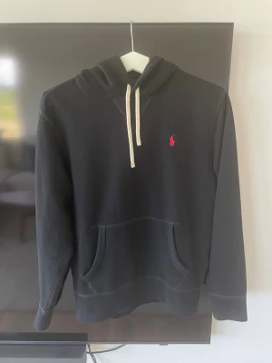 Svart hoodie med vita snören från Polo Ralph Lauren - Säljer en svart hoodie från Polo Ralph Lauren med vita snören och känguruficka framtill. På bröstet finns en liten röd broderad logga. Hoodien har huva och är tillverkad i mjukt material, perfekt för chill dagar. 9/10 skick. Självklart äkta. Tveka inte på att höra av dig vid frågor! Kan gå ner i pris.