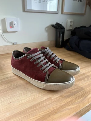 Vinröda sneakers med mockadetaljer - Snygga sneakers i vinröd mocka med grå snörning och olivgröna detaljer på tån och hälen. Skorna har en vit sula och en stilren design som passar perfekt till streetwear eller casual outfits. Priset går att diskutera! Hör av er vid intresse! Skickar samma dag eller dagen efter!