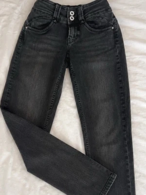 Svarta skinny jeans med dubbla knappar - Snygga svarta skinny jeans med dubbla vita knappar i midjan och klassiska fem fickor. Jeansen har en lätt tvättad look och smal passform som sitter tajt längs benen. Perfekta för dig som gillar en stilren och modern look.