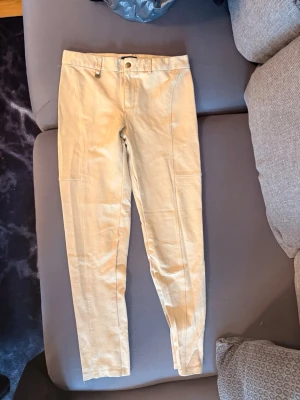 Beige byxor från Polo Ralph Lauren - Snygga beige byxor från Polo Ralph Lauren i storlek XL. Byxorna har raka ben, hög midja och klassisk design med knapp och dragkedja framtill. Tillverkade i ett mjukt och bekvämt material som passar perfekt till många olika stilar.