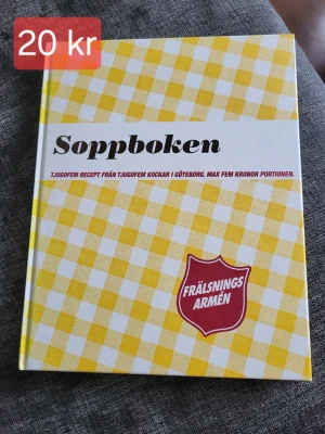 Soppboken Frälsningsarmén - En kokbok med titeln Soppboken, fylld med 25 sopprecept från olika kockar i Göteborg. Omslaget har ett gult och vitt rutigt mönster och Frälsningsarméns logga i rött. Perfekt för dig som vill laga billig och god soppa.