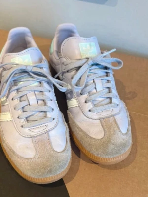 Adidas Samba lila sneakers - Snygga Adidas Samba sneakers i lila läder med klassiska vita ränder och detaljer i beige mocka framtill. Skorna har gummisula och lila skosnören. Perfekta för dig som gillar retrostil och vill sticka ut med en fräsch färg. Tecken på användning men väl omhändertagna