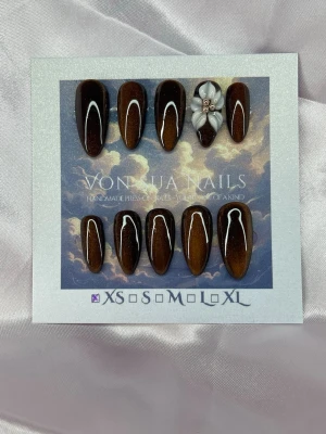 Chestnut (XS);Medium Almond - Snygga handgjorda press-on naglar i en medium lång mandelform med mörkbrun/glödande cateye bas. En nagel har en 3D-blomma i vitt med små champagnepärlor i mitten. Perfekt för dig som vill ha en unik och trendig look.XS: 14 mm, 11 mm, 11,5 mm, 10 mm, 8 mm