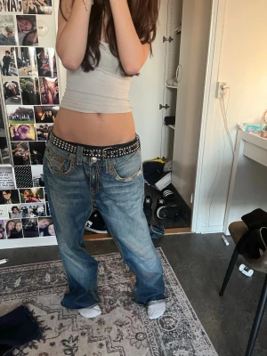 Baggy ljusblå jeans med nitar - Säljer ett par riktigt baggy ljusblå jeans med slitningar och tvättade detaljer. Jeansen har låg midja och vida ben, samt coola nitar på fickorna och en bred bältesögla. Perfekta för en avslappnad och trendig streetwear-look.