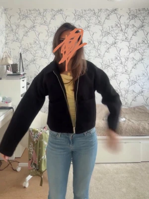 Svart zip cardiganjacka i fleece - Mysig svart cardiganjacka i fleece med dragkedja framtill och två stora fickor. Jackan har en croppad passform och långa ärmar, perfekt att slänga över en t-shirt eller topp. Enkel och stilren design som passar till jeans eller kjol.