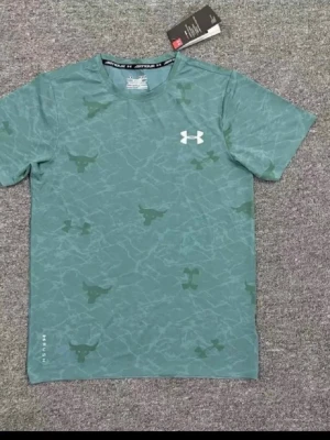 Grön mönstrad t-shirt från Under Armour - Snygg grön t-shirt från Under Armour med diskret mönster och logga på bröstet. Tillverkad i ett lätt och funktionellt material som passar perfekt till träning. Klassisk passform och rund halsringning.