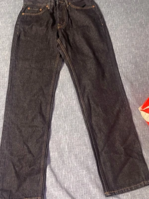 Mörkblå raka jeans med kontrastsömmar - Säljer ett par mörkblå jeans med raka ben och klassisk femficksmodell. Jeansen har kontrastsömmar i gult och silverfärgade nitar. Materialet är kraftig denim som ger en tidlös look. Perfekta till vardagsstilen och funkar året runt.
