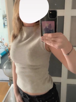 Beige ribbad ärmlös topp - Säljer en beige, ribbad topp med hög hals och ärmlös design. Toppen har en croppad passform och är tillverkad i ett mjukt material som sitter snyggt mot kroppen. Perfekt för dig som gillar stilrena och enkla plagg.