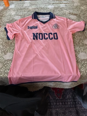 NOCCO Fotbollströja L  - Säljer en rosa fotbollsträja från nocco Med Tropical på ryggen och nummer 26. Helt ny oanvänd. Storlek L 