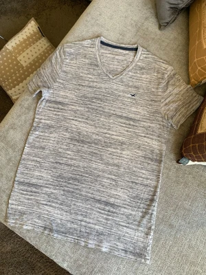 Gråmelerad t-shirt med v-ringning - Snygg gråmelerad t-shirt med v-ringning och diskret logga på bröstet. T-shirten har korta ärmar och är tillverkad i mjukt material som känns skönt mot huden. Perfekt till jeans eller shorts för en avslappnad look.